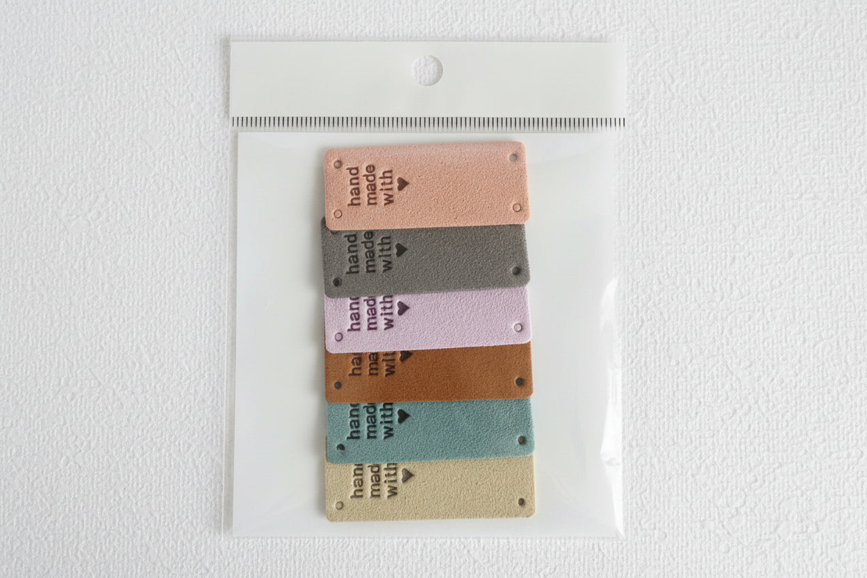 Set of five fabric tags 'hand-made with love', different colors with text on a clear plastic backing.