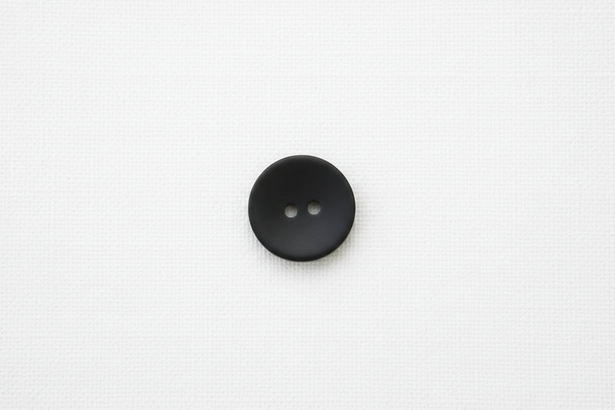 Black matte button with two holes on a white background