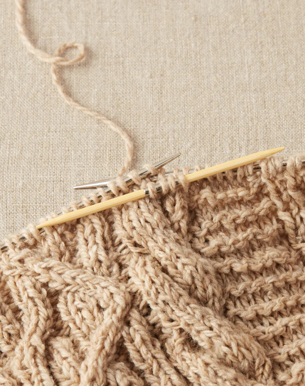 Knitted fabric with wooden cable needles on a beige background