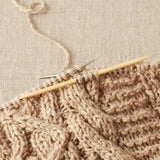 Knitted fabric with wooden cable needles on a beige background