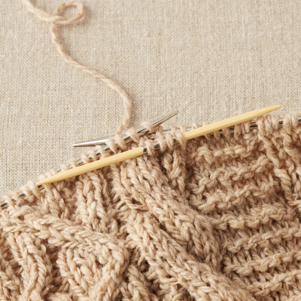 Knitted fabric with wooden cable needles on a beige background
