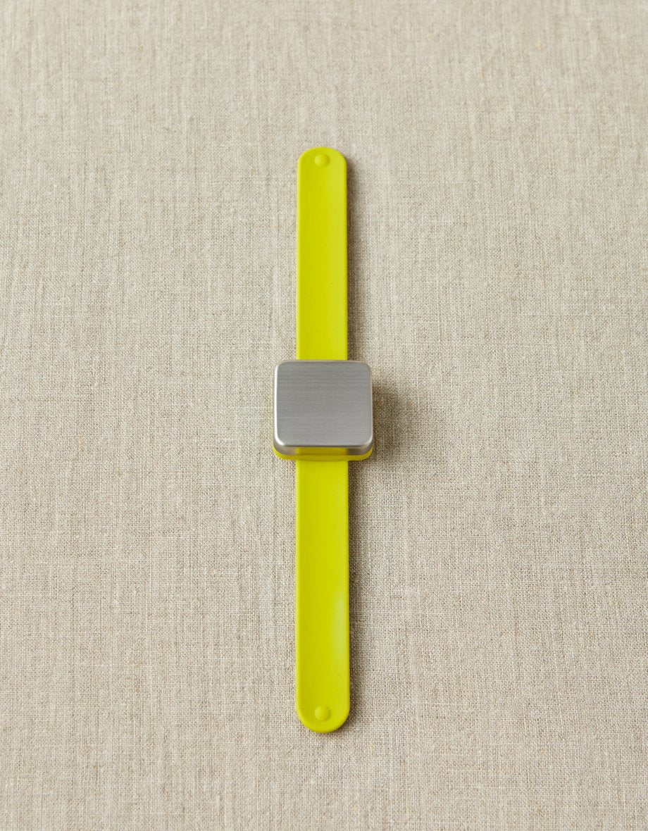 Yellow notions holder bracelet with a square magnet on a beige fabric background