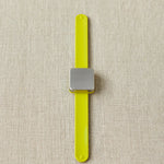 Yellow notions holder bracelet with a square magnet on a beige fabric background