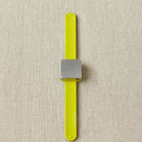 Yellow notions holder bracelet with a square magnet on a beige fabric background