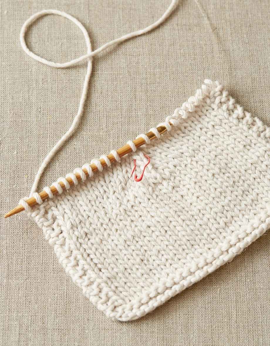 Knitted fabric with an opening stitch marker used on a beige fabric background