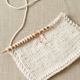Knitted fabric with an opening stitch marker used on a beige fabric background