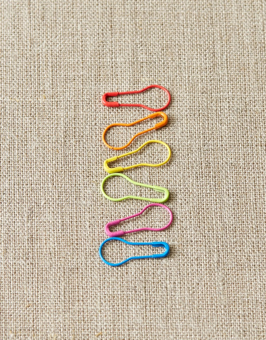 Colorful safety pin stitch markers arranged in a pattern on a textured beige background