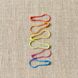 Colorful safety pin stitch markers arranged in a pattern on a textured beige background