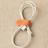 White USB cable with an orange magnetic clip labeled 'Cocoknits' on a beige fabric background