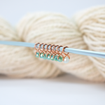 Knitting needle with decorative beaded stitch markers against a yarn ball on a light background