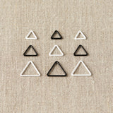 Set of triangle-shaped stitch markers on a beige fabric background