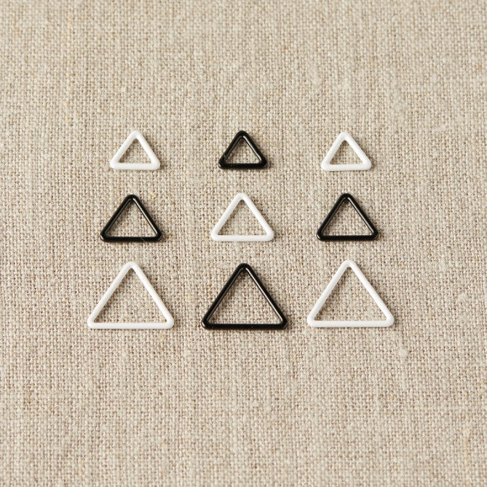 Set of triangle-shaped stitch markers on a beige fabric background