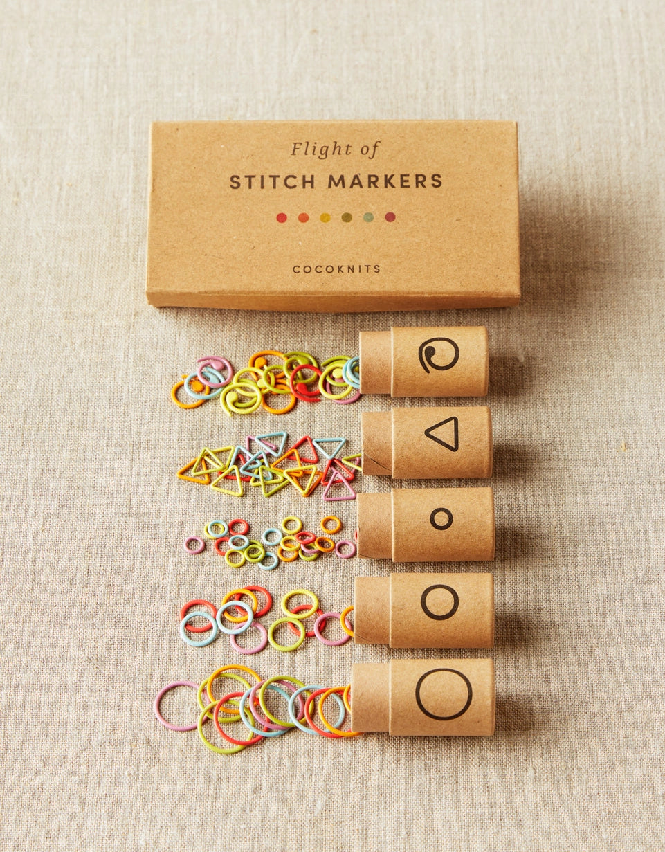 Set of stitch markers with a cardboard box on a beige fabric background