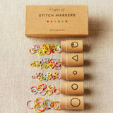Set of stitch markers with a cardboard box on a beige fabric background