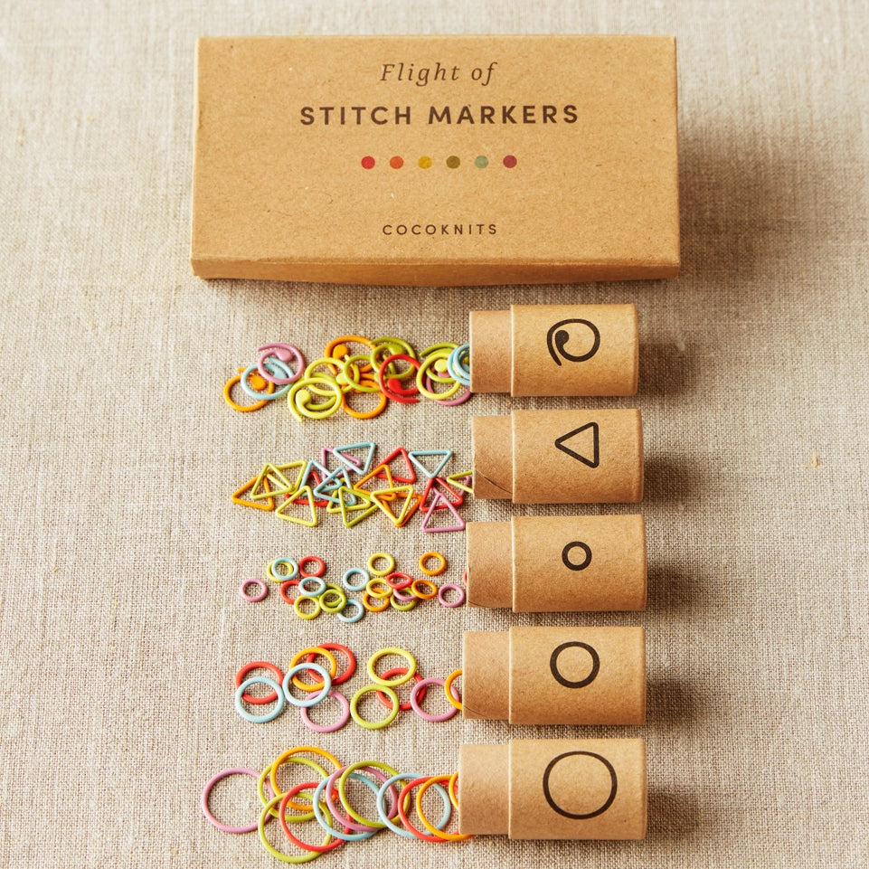 Set of stitch markers with a cardboard box on a beige fabric background