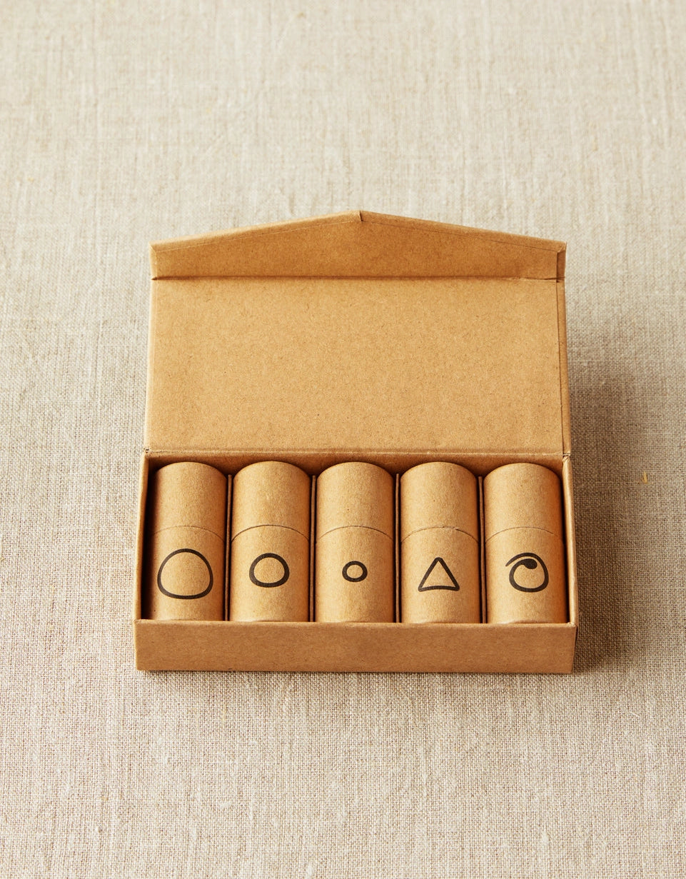 Set of five cylindrical containers with notions symbols on a cardboard box against a beige textured background
