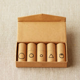Set of five cylindrical containers with notions symbols on a cardboard box against a beige textured background