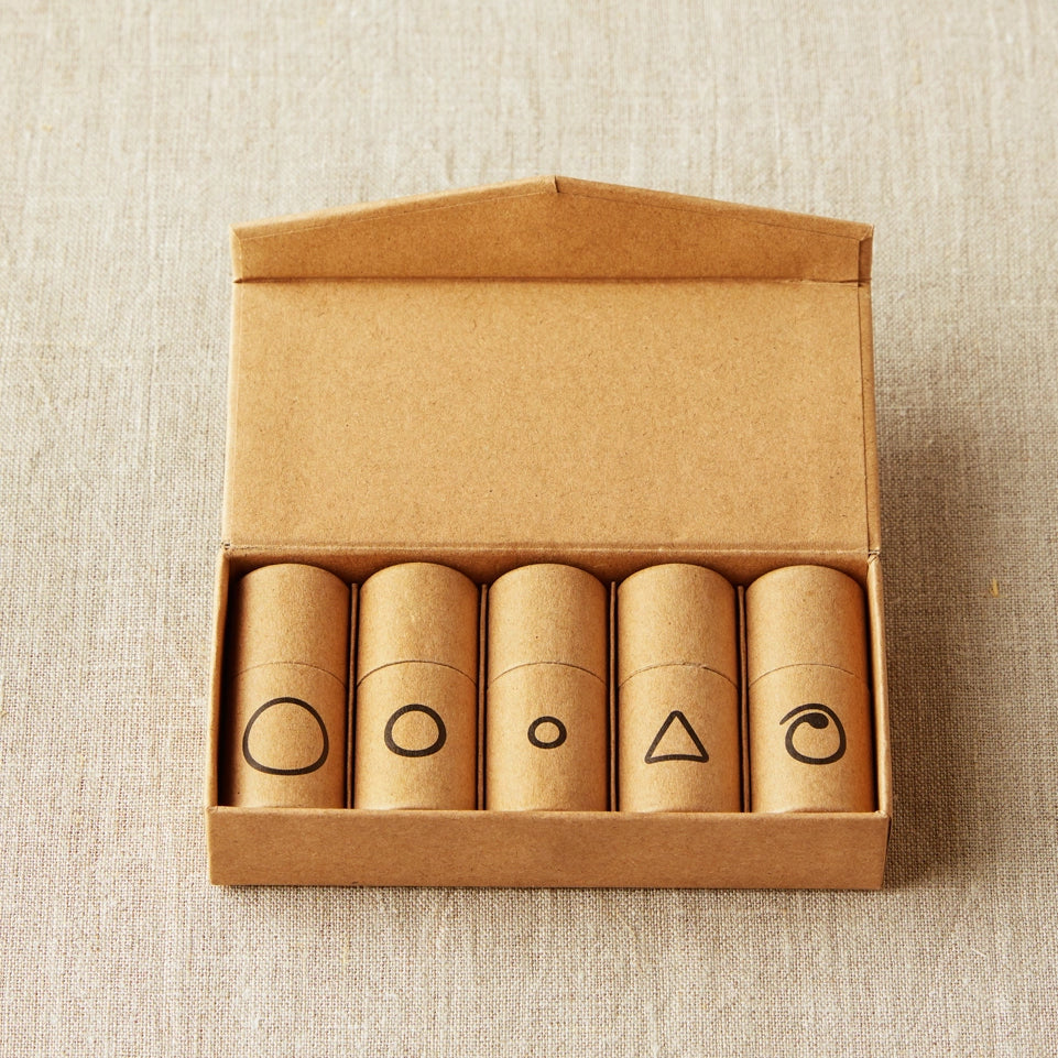 Set of five cylindrical containers with notions symbols on a cardboard box against a beige textured background