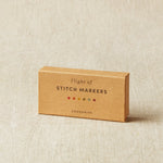 Box of stitch markers on a beige fabric background