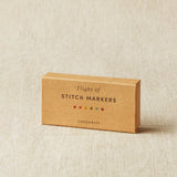 Box of stitch markers on a beige fabric background