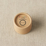 Round wooden container with 'jumbo stitch markers' label on a beige fabric background