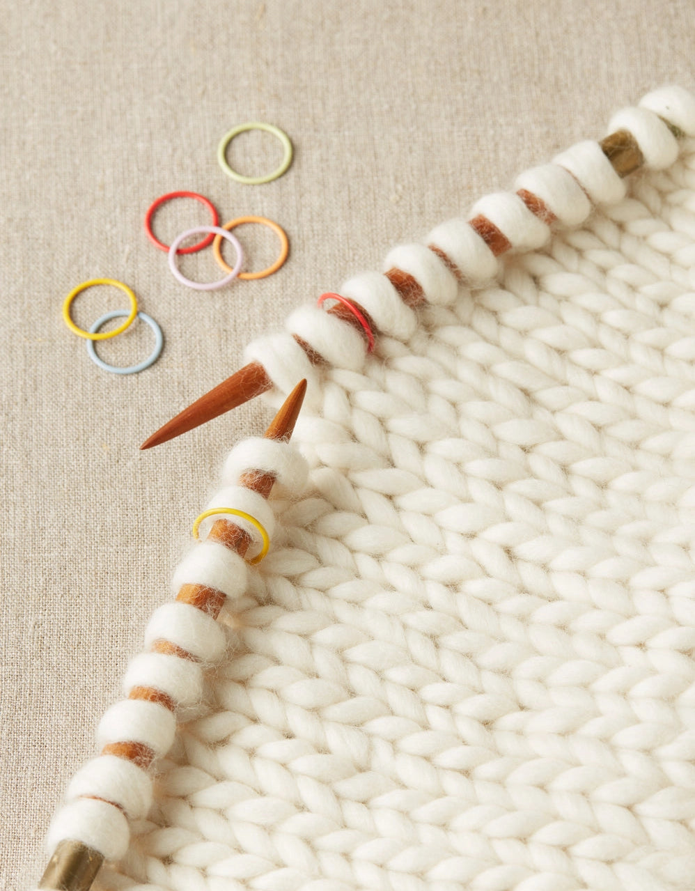Knitting needles with jumbo stitch markers on a knitted fabric background