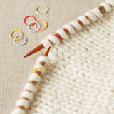 Knitting needles with jumbo stitch markers on a knitted fabric background