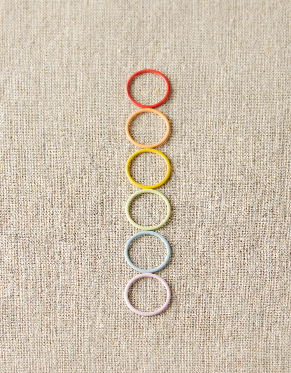 Colorful ring stitch markers arranged vertically on a textured beige background