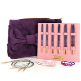 Purple clutch bag with a bow, pink case holding knitting needles, and additional needles on a white background