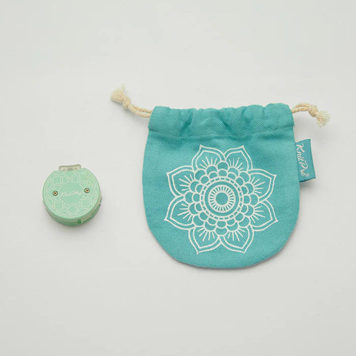 Turquoise pouch with white mandala design and small green item on a light gray background