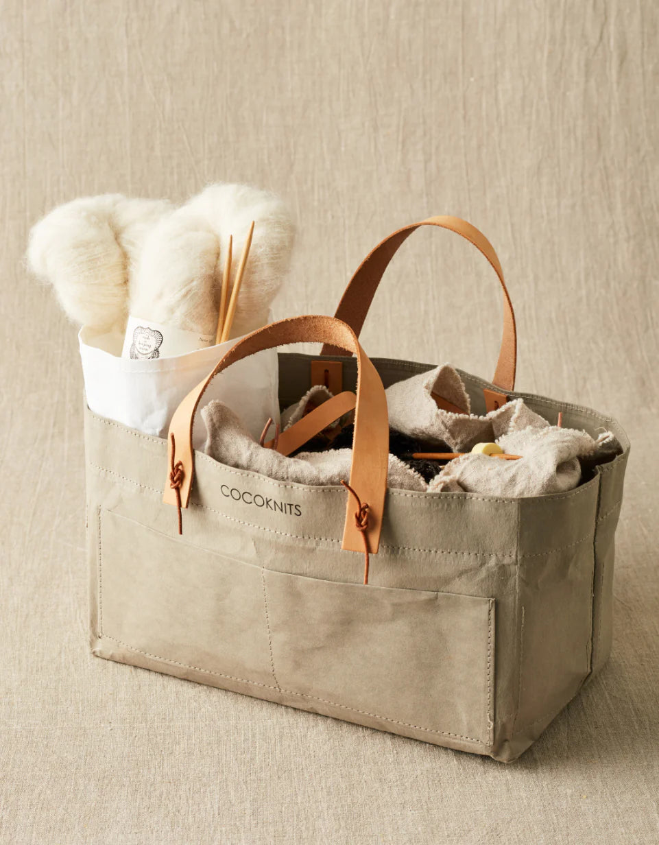 Beige tote bag with leather handles filled with items on a beige background