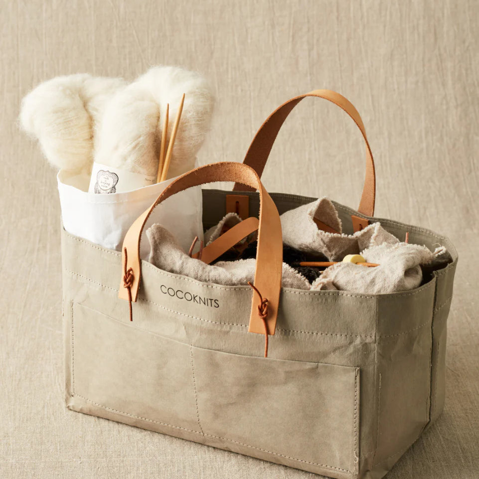 Beige tote bag with leather handles filled with items on a beige background