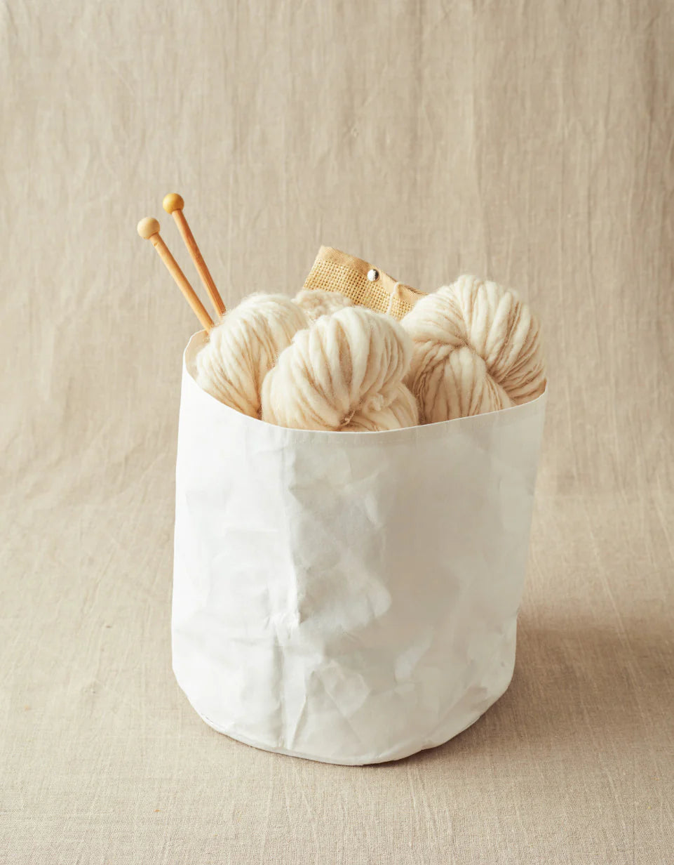 White yarn balls with knitting needles in a white container on a beige background