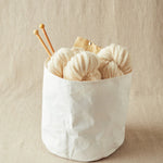 White yarn balls with knitting needles in a white container on a beige background