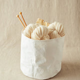 White yarn balls with knitting needles in a white container on a beige background