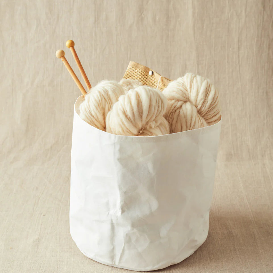 White yarn balls with knitting needles in a white container on a beige background