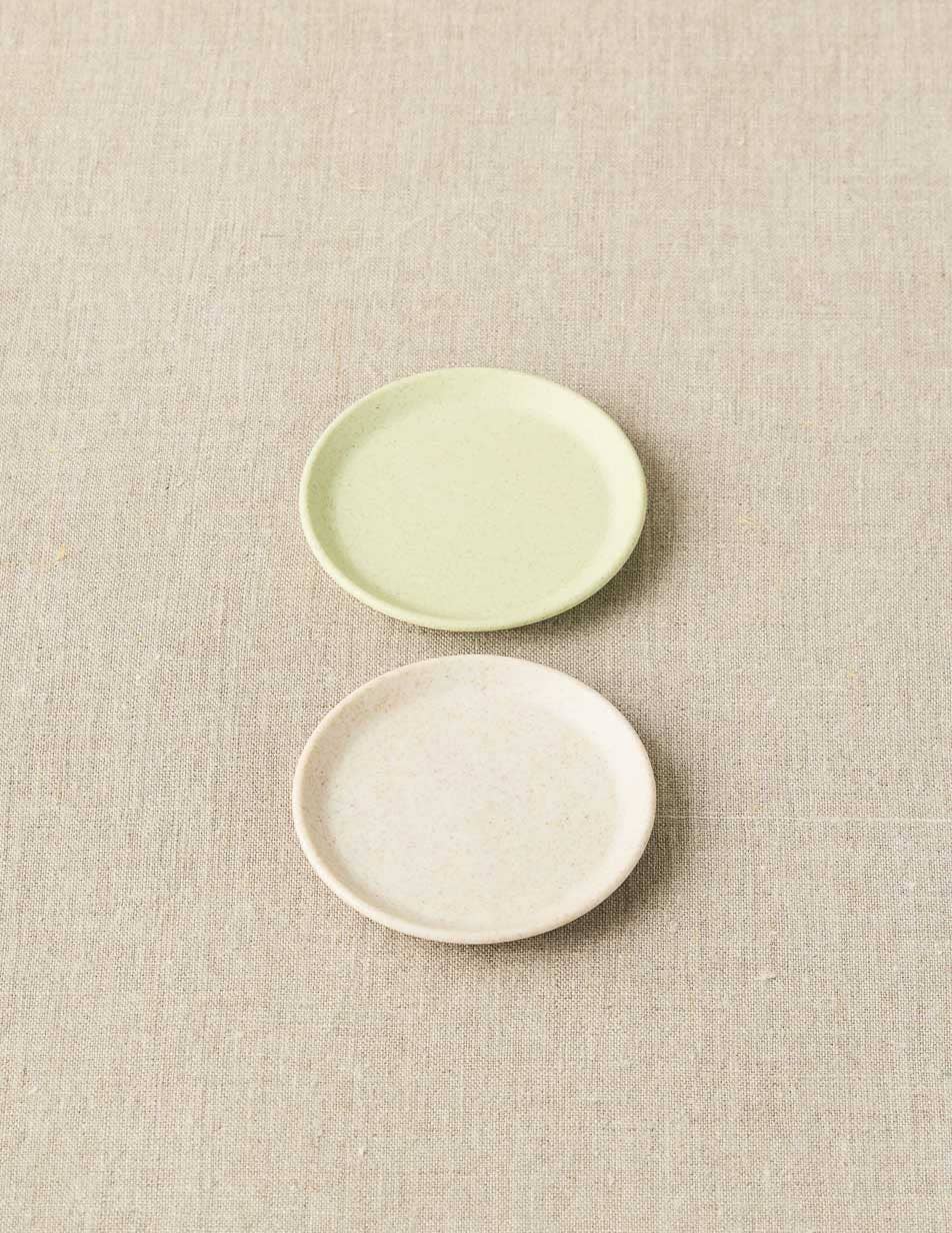 Two ceramic plates, one green and one white, on a textured beige surface.