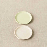 Two ceramic plates, one green and one white, on a textured beige surface.