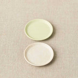 Two ceramic plates, one green and one white, on a textured beige surface.