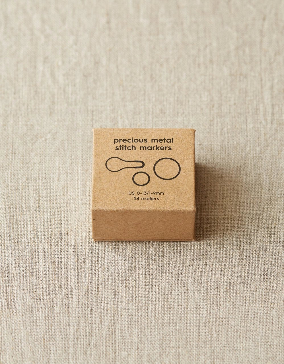 Box of precious metal stitch markers on a beige fabric background