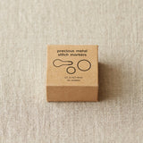Box of precious metal stitch markers on a beige fabric background