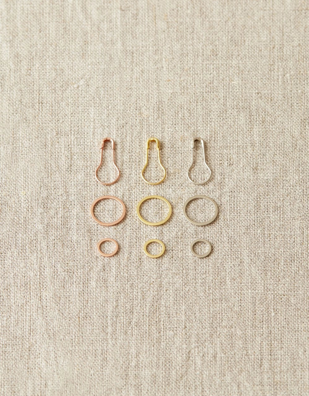 Set of metal ring and opening stitch markers on a beige fabric background