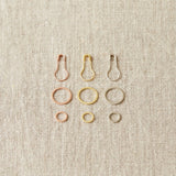 Set of metal ring and opening stitch markers on a beige fabric background