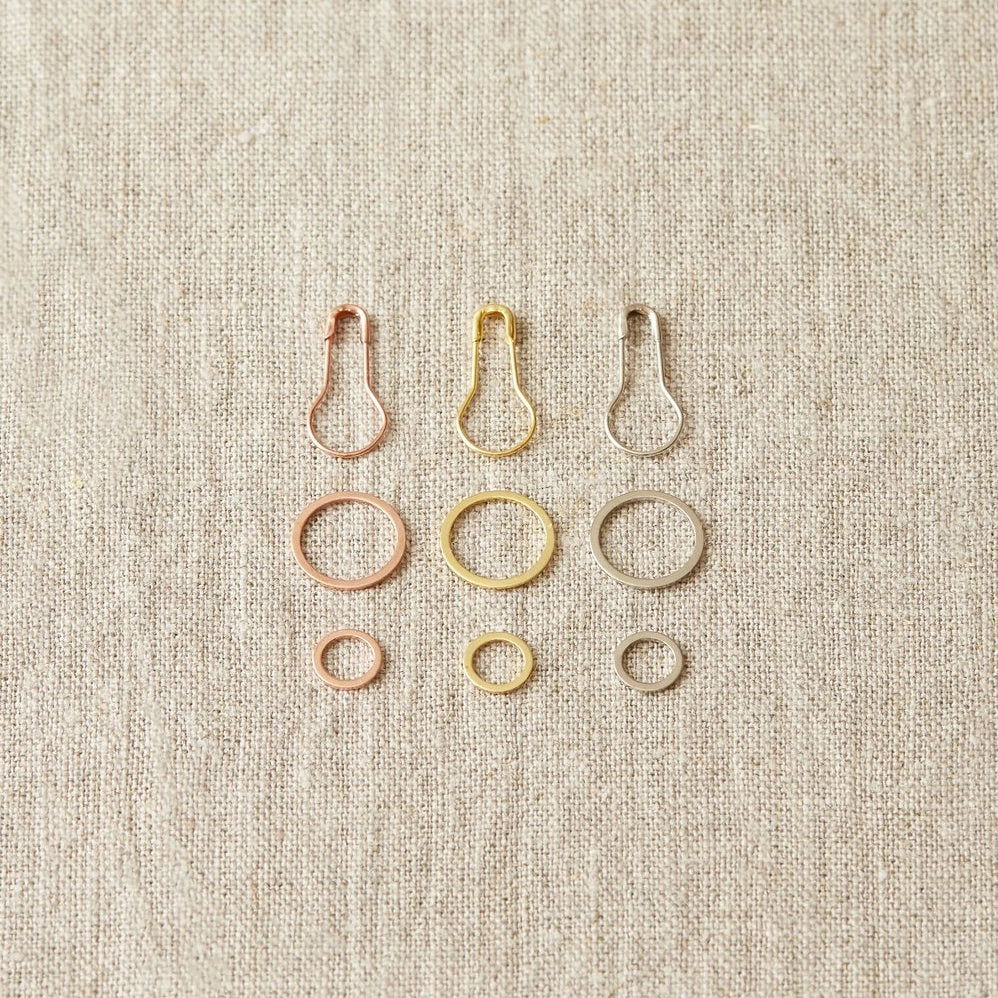 Set of metal ring and opening stitch markers on a beige fabric background