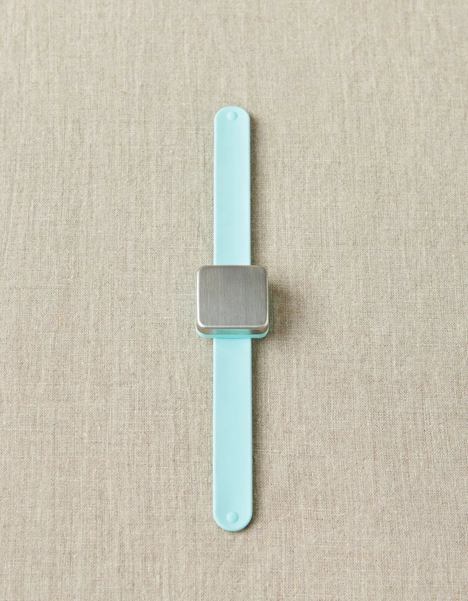 Slap bracelet with a square magnet with a light blue strap on a beige fabric background