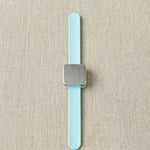 Slap bracelet with a square magnet with a light blue strap on a beige fabric background