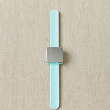 Slap bracelet with a square magnet with a light blue strap on a beige fabric background