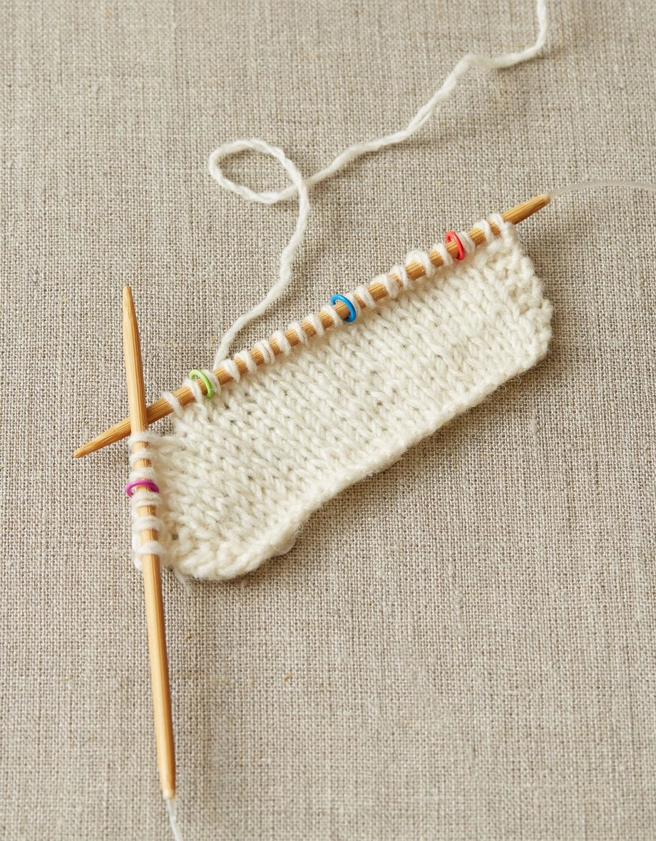Knitted fabric with wooden knitting needles using small stitch markers on a textured beige background