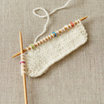 Knitted fabric with wooden knitting needles using small stitch markers on a textured beige background