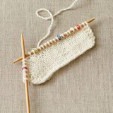 Knitted fabric with wooden knitting needles using small stitch markers on a textured beige background